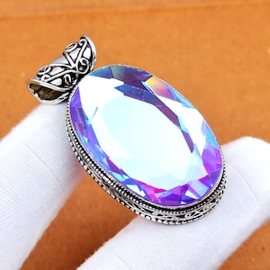 Puede incluir: Colgante ovalado con una gran piedra preciosa iridiscente. La piedra preciosa muestra una gama de colores, incluyendo azul, púrpura y rosa. El colgante está engastado en un metal plateado con detalles intrincados en los bordes y una fianza decorativa. Mide unos 4 cm de largo.