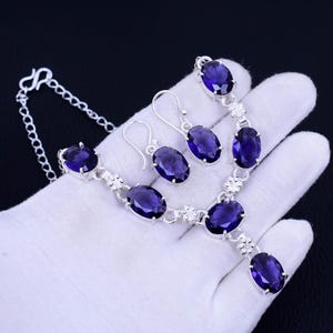 May include: A silver necklace and earrings set with oval-shaped amethyst gemstones. The necklace has a delicate chain and a pendant with a larger amethyst stone. The earrings are simple and elegant, with a single amethyst stone hanging from each.