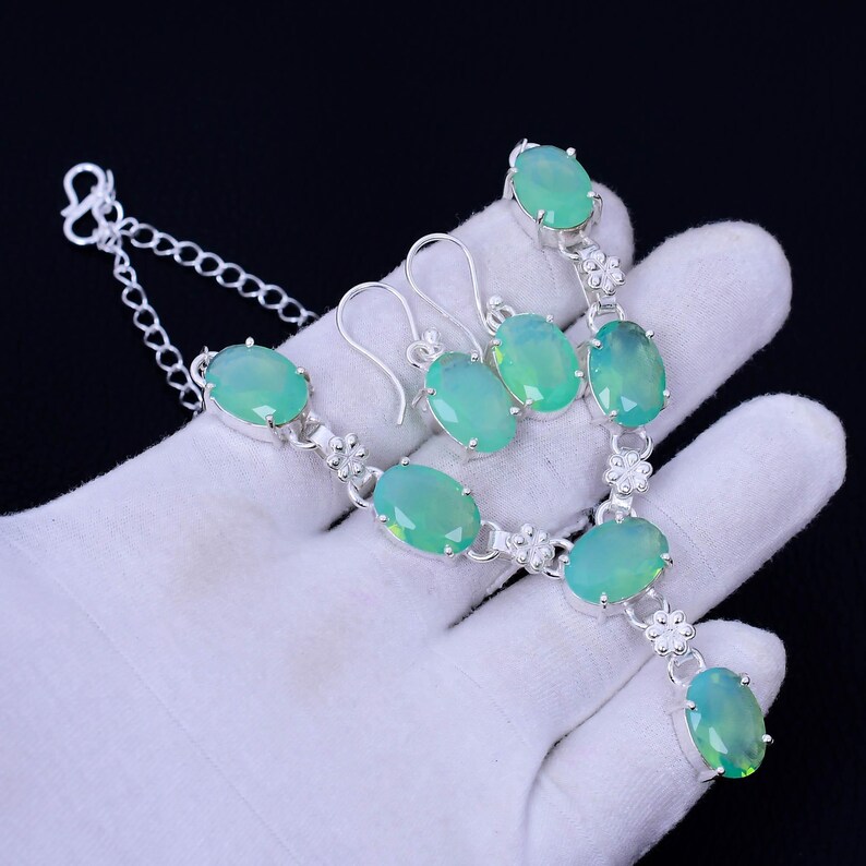 K&ouml;nnte beinhalten: Ein silbernes Halsketten- und Ohrring-Set mit gr&uuml;nen ovalen Edelsteinen. Die Halskette hat einen Anh&auml;nger mit einem gr&ouml;&szlig;eren Edelstein und eine Kette mit einem Karabinerverschluss.