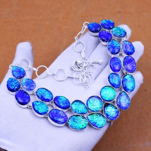 Könnte beinhalten: Halskette aus Silber mit ovalen Steinen aus blauem und türkisem dichroitischem Glas. Die Steine sind mit einer Silberkette und einem Verschluss verbunden. Das Glas hat einen schimmernden, irisierenden Effekt.