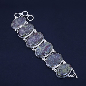 Può includere: Un braccialetto d'argento con sei pietre ovali di colore verde, rosso e nero. Il braccialetto ha una chiusura a scatto.