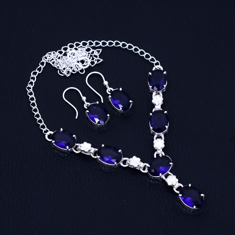 May include: A silver necklace and earrings set with a silver chain and oval-shaped blue gemstones.