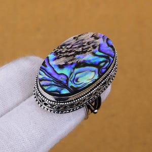 May include: A silver ring with an oval abalone shell inlay. The shell has a swirling pattern of blue, green, and purple.