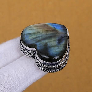 Könnte beinhalten: Ein silberner Herzring mit einem blauen und grünen Labradorit-Edelstein. Der Ring hat ein filigranes Silberdesign am Rand.