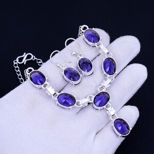 May include: A silver necklace and earrings set with purple oval-shaped gemstones. The necklace has a pendant with a larger purple gemstone.