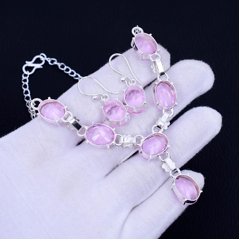 May include: A silver necklace and earrings set with pink oval-shaped stones. The necklace has a pendant with a larger pink stone.