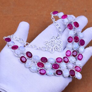 May include: A silver necklace featuring alternating oval-shaped ruby and moonstone gemstones. The necklace is composed of multiple strands connected by a silver chain. The gemstones are set in silver bezels.