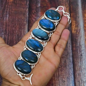 Könnte beinhalten: Ein silbernes Armband mit sechs ovalen Labradorit-Edelsteinen. Die Steine sind tiefblau mit schillernden Farbeffekten. Das Armband hat einen Karabinerverschluss.