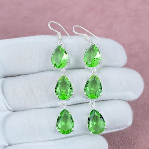 May include: A pair of silver dangle earrings with three pear-shaped green gemstones on each earring.