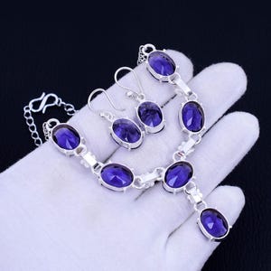 May include: A silver necklace and earrings set with purple oval-shaped gemstones. The necklace has a pendant with a larger purple gemstone.