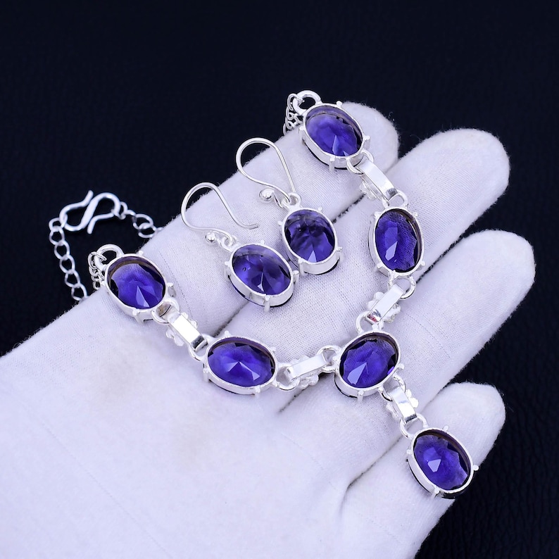 May include: A silver necklace and earrings set with purple oval-shaped gemstones. The necklace has a pendant with a larger purple gemstone.