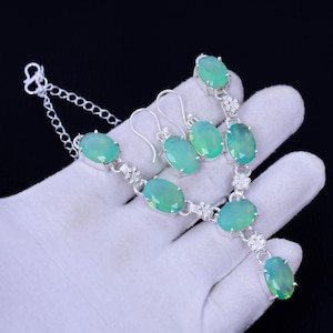 K&ouml;nnte beinhalten: Ein silbernes Halsketten- und Ohrring-Set mit gr&uuml;nen ovalen Edelsteinen. Die Halskette hat einen Anh&auml;nger mit einem gr&ouml;&szlig;eren Edelstein und eine Kette mit einem Karabinerverschluss.