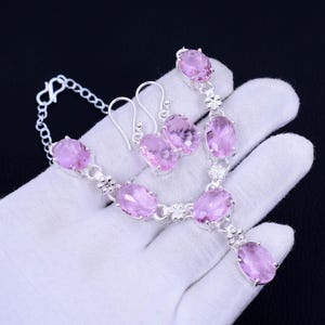 May include: A silver necklace and earrings set with pink oval-shaped gemstones. The necklace has a delicate chain and a pendant with a larger gemstone. The earrings are drop earrings with smaller gemstones.