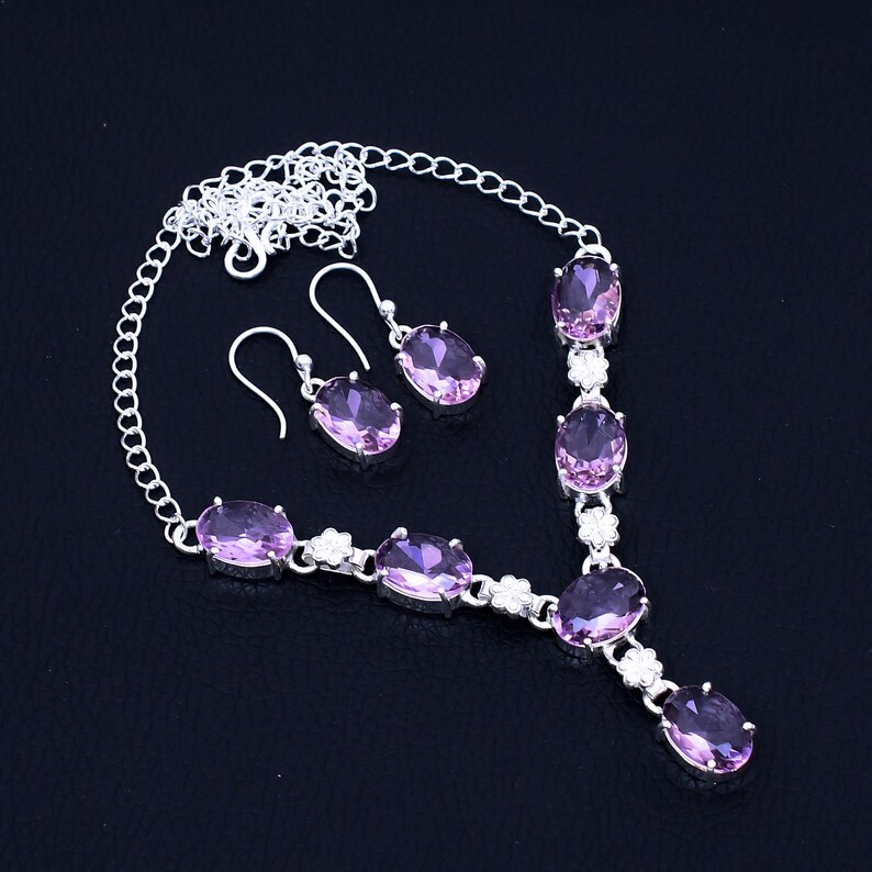 May include: A silver necklace and earrings set with oval-shaped pink gemstones. The necklace features a delicate chain with a pendant and multiple gemstones.