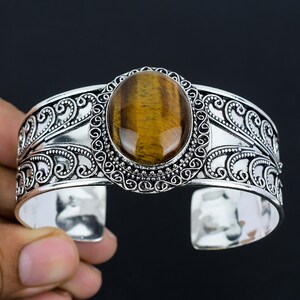 May include: Silver cuff bracelet with an ornate design and a large oval tiger's eye gemstone.