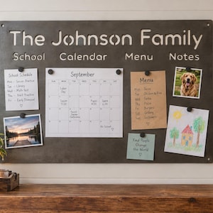 Könnte beinhalten: Eine rechteckige, dunkelgraue magnetische Metall-Wandtafel mit dem lasergeschnittenen Text The Johnson Family sowie den Überschriften School, Calendar, Menu und Notes. Die Tafel zeigt verschiedene Papiere, einen Kalender und Fotos, die mit Magneten befestigt sind.