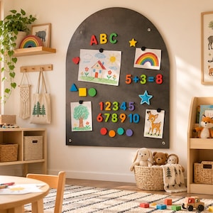 May include: A large, arched, dark gray magnetic wall board featuring colorful plastic letters, numbers, and geometric shapes. The board displays children's drawings of a house and a tree, a rainbow illustration, and the math equation 5+3=8.
