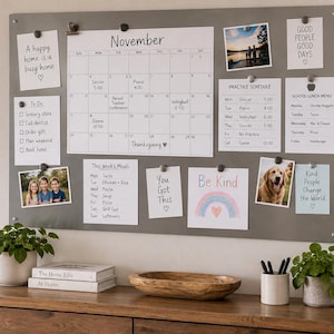 Peut inclure: Un grand tableau magnétique mural rectangulaire gris affichant un calendrier de novembre, une liste de tâches, un planning d'entraînement, un menu scolaire, un menu hebdomadaire, des photos et des notes fixées par des aimants noirs.