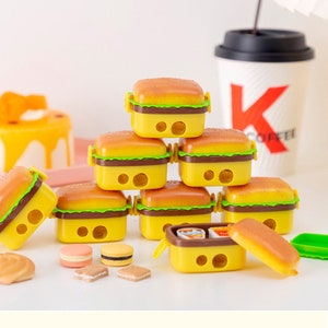 Könnte beinhalten: Ein Stapel gelber und brauner Bleistiftspitzer in Form von Hamburgern. Die Spitzer haben zwei Löcher zum Anspitzen von Bleistiften. Auf dem Tisch liegen auch kleine Kekse und Macarons.