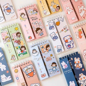 May include: A selection of colourful spiral-bound notebooks with cartoon illustrations. The notebooks feature bears, bunnies, and girls, with text in English and Japanese. The notebooks are in shades of pink, blue, green, and yellow.