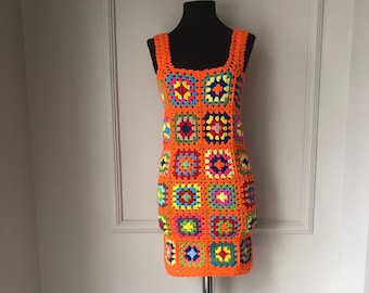 May include: An orange crochet dress displayed on a mannequin. The dress features a square neckline and is constructed from colorful, square crochet patches. The squares are in various colors, including pink, blue, yellow, and green.