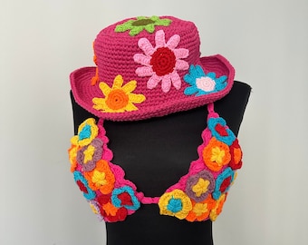 May include: A pink crocheted hat with colorful flower embellishments. The hat is on a black mannequin. The mannequin is also wearing a colorful crocheted top with flower embellishments.