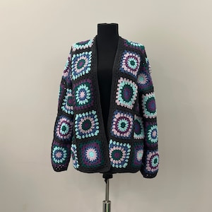 May include: A black crocheted cardigan with a granny square pattern in shades of purple, teal, and light blue.
