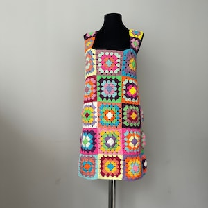 May include: A colorful crochet dress with a square pattern in shades of pink, purple, orange, yellow, green, and blue.