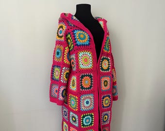 May include: A long, pink crocheted cardigan with a hood. The cardigan is made of colorful squares with a variety of patterns.