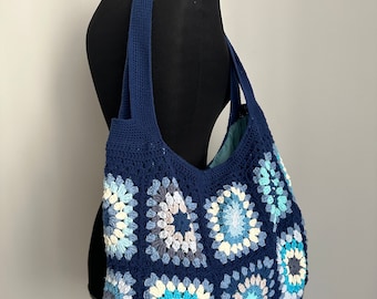 May include: A navy blue crocheted tote bag with a large, colorful granny square design. The bag has two long straps and a wide opening.