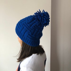 May include: A blue knitted beanie with a pom pom on top. The beanie has a cable knit pattern.