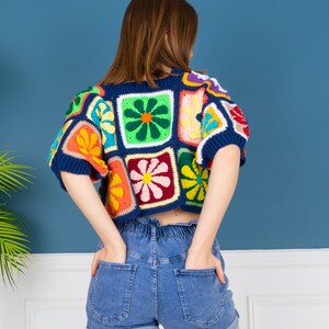 May include: A colorful crochet top with a patchwork design featuring flowers in various colors. The top is cropped and has short sleeves.