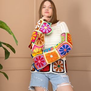 May include: A white crochet top with colorful floral patterned sleeves and a white crochet bodice. The top is paired with light blue denim shorts.