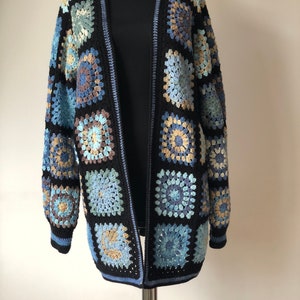 May include: A long black cardigan with a crocheted design featuring blue, brown and beige squares.