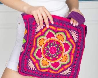 May include: A crocheted bag with a colorful floral design in shades of pink, orange, green, and purple. The bag has a single strap and is made with a chunky yarn.