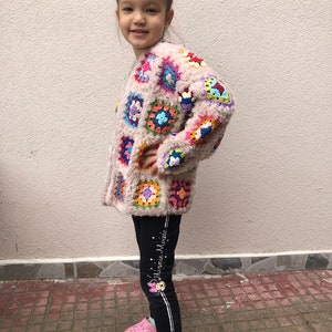 May include: A young person wearing a pink crocheted cardigan with colorful squares and black leggings with white stripes and the text "Minnie Mouse".