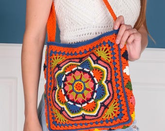 May include: A colorful crocheted tote bag with a floral design in shades of orange, blue, green, yellow, pink, and white. The bag has a long orange strap.