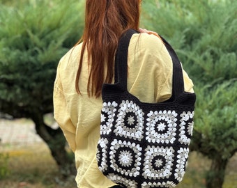 May include: A black and white crocheted tote bag with a square pattern. The bag has a single strap and is worn over the shoulder.