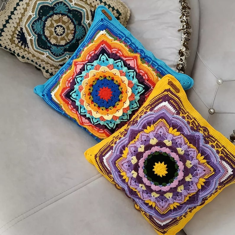 May include: Three square crochet cushions with detailed mandala patterns. The cushions display bright colours such as blue, orange, yellow, and purple. Each cushion has a unique design and texture, adding a decorative touch to any room.