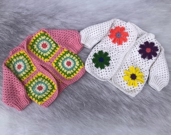 May include: Two crocheted baby cardigans, one pink with green and white flowers and one white with colourful flowers.