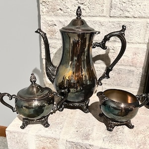 May include: A silver tea set with a teapot, creamer, and sugar bowl. The set has a traditional design with ornate handles and a polished finish.