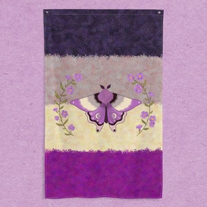 May include: A purple, white, and gray flag with a moth design in the center. The moth is surrounded by a wreath of purple flowers. The flag is made of fabric and has a textured look.