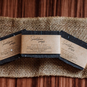 May include: Three bars of black charcoal soap with brown paper labels that read "Sweetbriar Soaps" and "Charcoal Face Soap Handcrafted Eco-Friendly Soap Made with Natural Skin-Loving Ingredients".