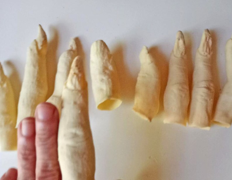 May include: A set of eight realistic-looking, pale yellow, finger-shaped props. The props are made of a soft, pliable material and are arranged in a row on a white surface.