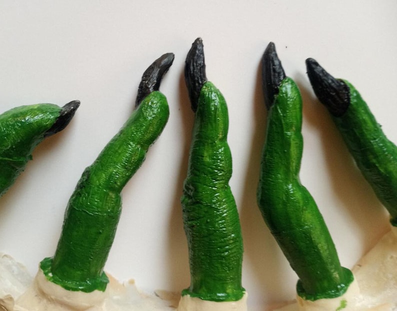 May include: Five green and black finger props with pointed tips. The fingers are made of a soft, flexible material and are designed to look like claws.