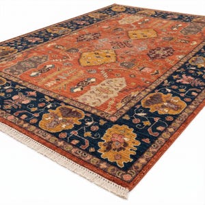 May include: An area rug with a central terracotta field and a navy blue border. The rug features intricate floral and geometric patterns in shades of gold, brown, and cream. The rug has a fringed edge.