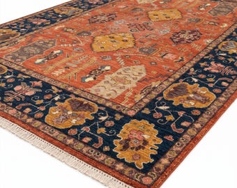 May include: An area rug with a central terracotta field and a navy blue border. The rug features intricate floral and geometric patterns in shades of gold, brown, and cream. The rug has a fringed edge.