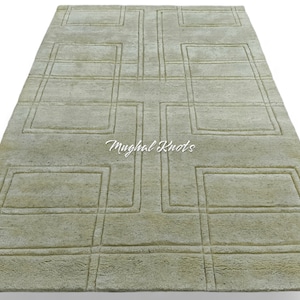 Puede incluir: Una alfombra verde claro con un patrón geométrico de cuadrados y rectángulos en relieve. La alfombra tiene un aspecto desgastado sutil y el texto "Mughal Knots" está impreso en el centro.