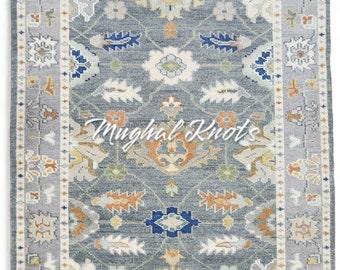 May include: A gray rug with a floral pattern in shades of blue, yellow, orange, and white. The rug has a border with a repeating pattern of small flowers and leaves. The text "Mughal Knots" is printed in the center of the rug.