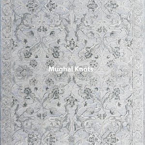 May include: A gray and white rug with a floral pattern. The rug has a border with a repeating pattern. The text "Mughal Knots" is in the center of the rug.